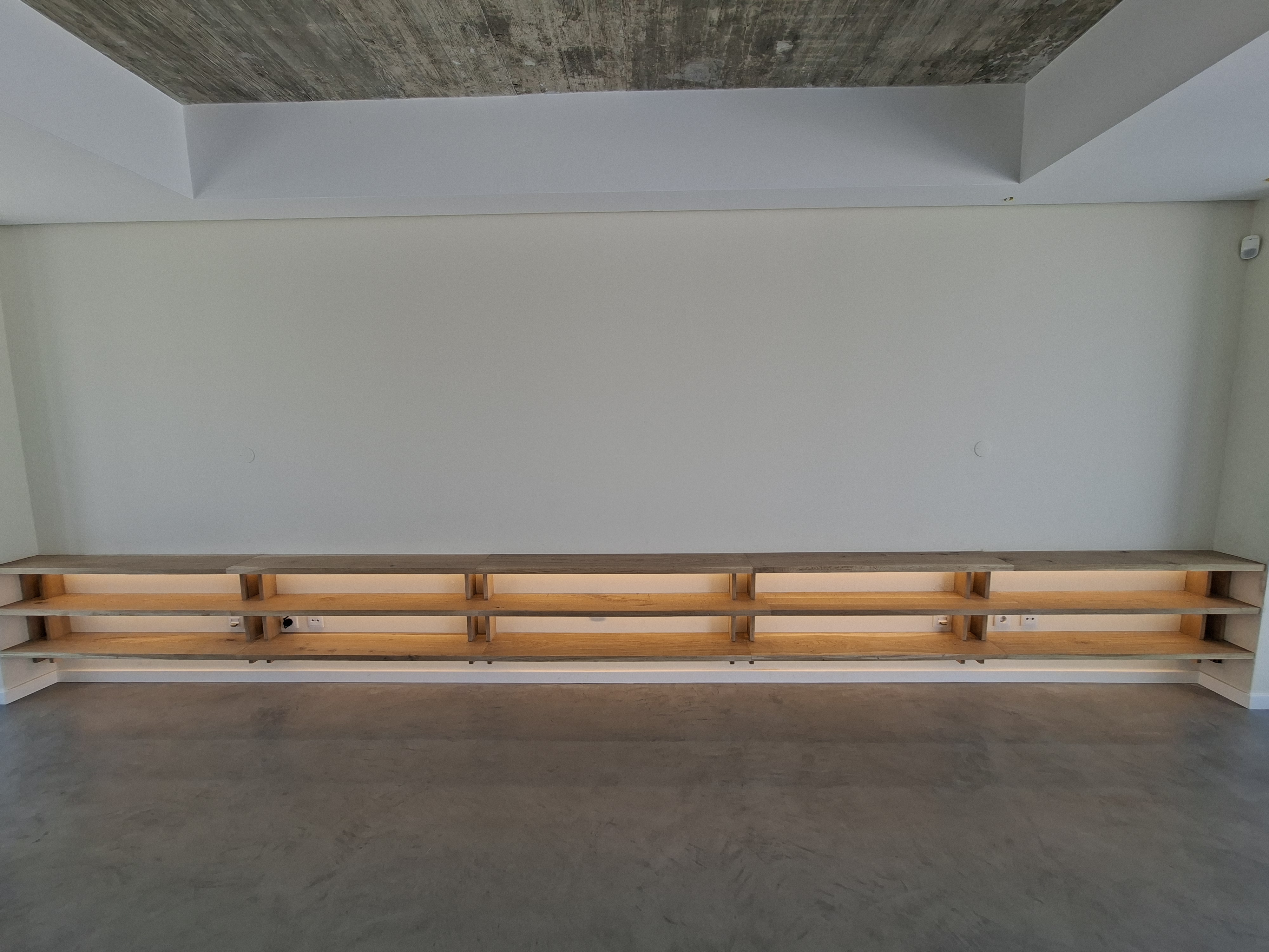 Bespoke carpentry project – Custom wall-to-wall floating oak shelving with integrated warm lighting in a modern interior space